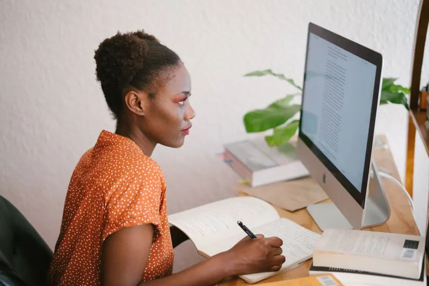 Woman in her thirties studying at a desk with notebooks and a computer, preparing for a competitive exam